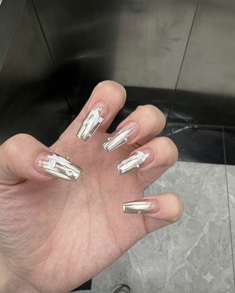 Hand angled to show the reflective mirror-like finish of silver chrome coated nails under indoor lighting.