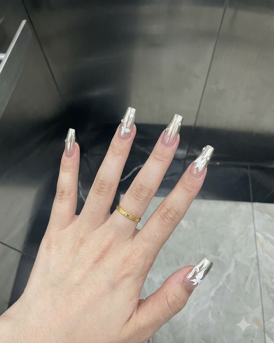 Detailed close-up of a finger showing a white butterfly decal applied over a silver chrome nail.