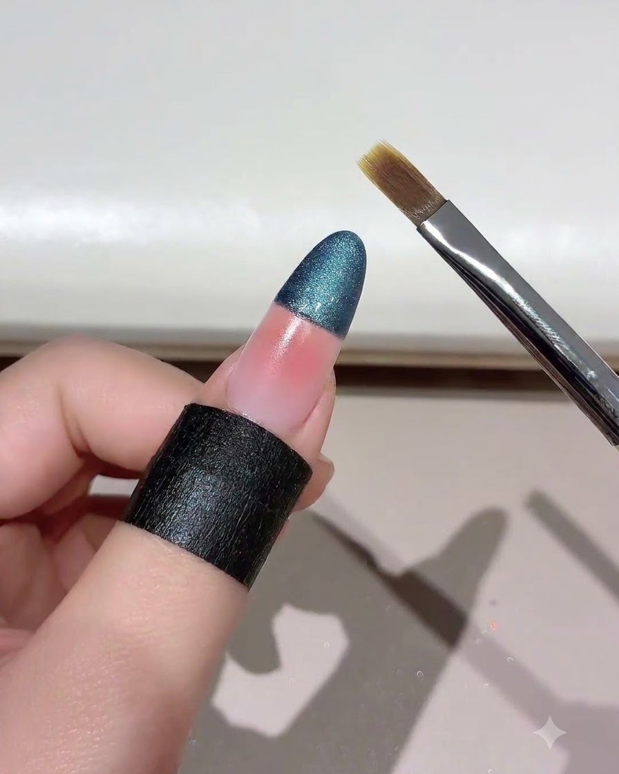 A nail brush held at an angle near a gradient-blended cat eye nail.