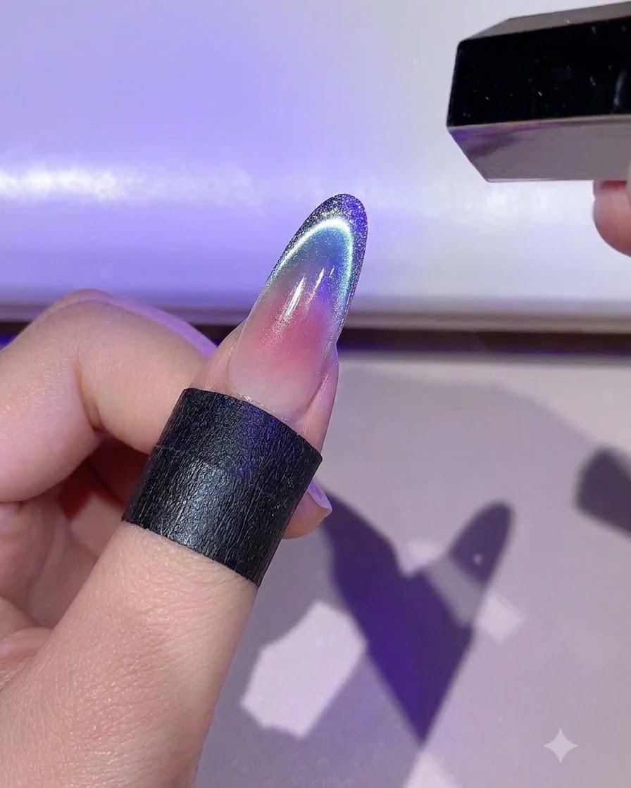 A hand holding a mini LED lamp curing the detailed gold gel outline on a fingernail.