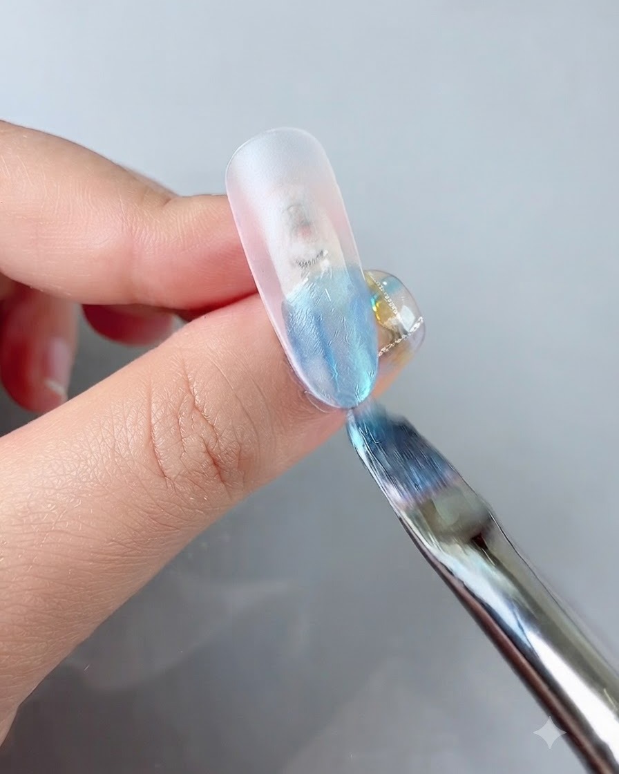 A nail brush applying a vibrant blue color gel to the tip of a clear nail extension.