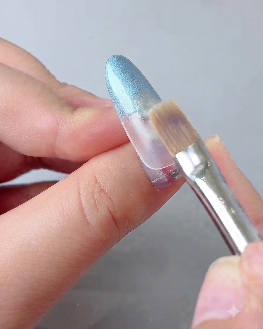 A blending brush softly smoothing the transition of blue gel on a nail.