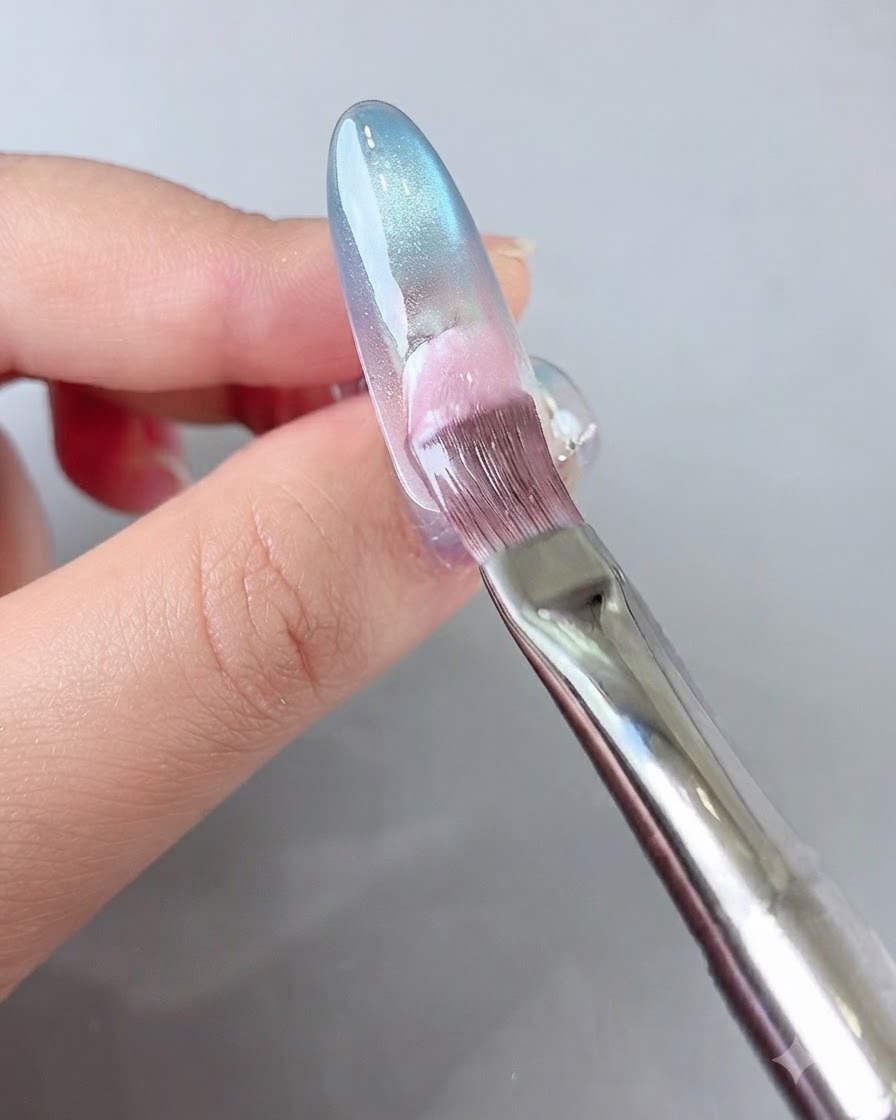 A brush applying pink gel to the back portion of the nail.