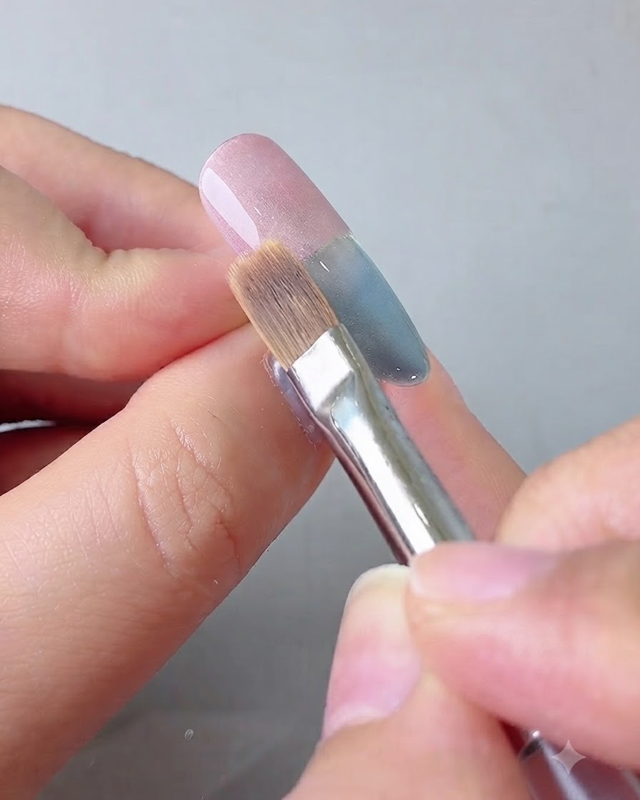A blending brush feathering the pink gel towards the center of the nail.