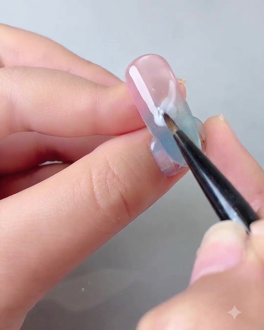 A fine detail brush applying milky white self-leveling gel in a soft cloud shape on a gradient nail.