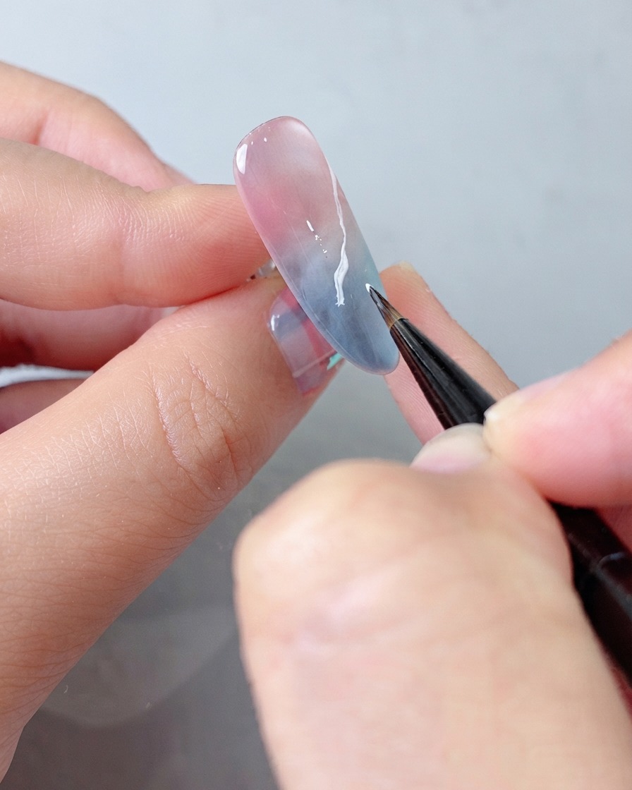 A detail brush applying an additional layer of white gel to the cloud pattern for enhanced depth.