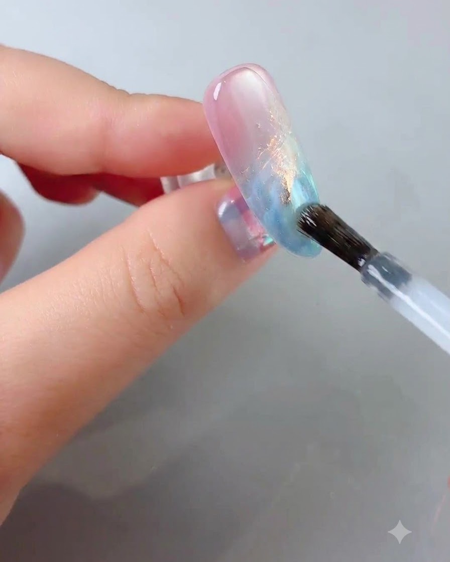 A nail brush gliding a clear glossy top coat over the decorated nail surface.