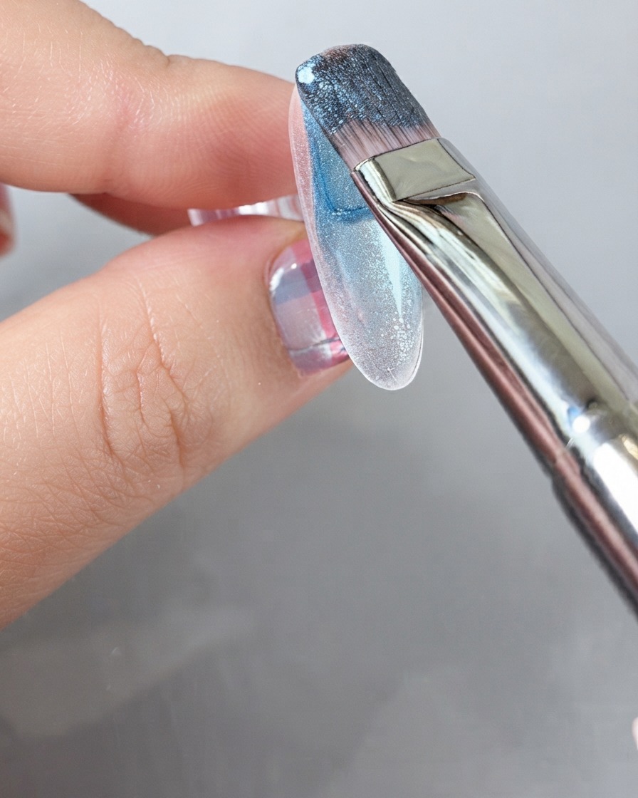 A brush applying a rich blue gel polish across the entire surface of a nail.