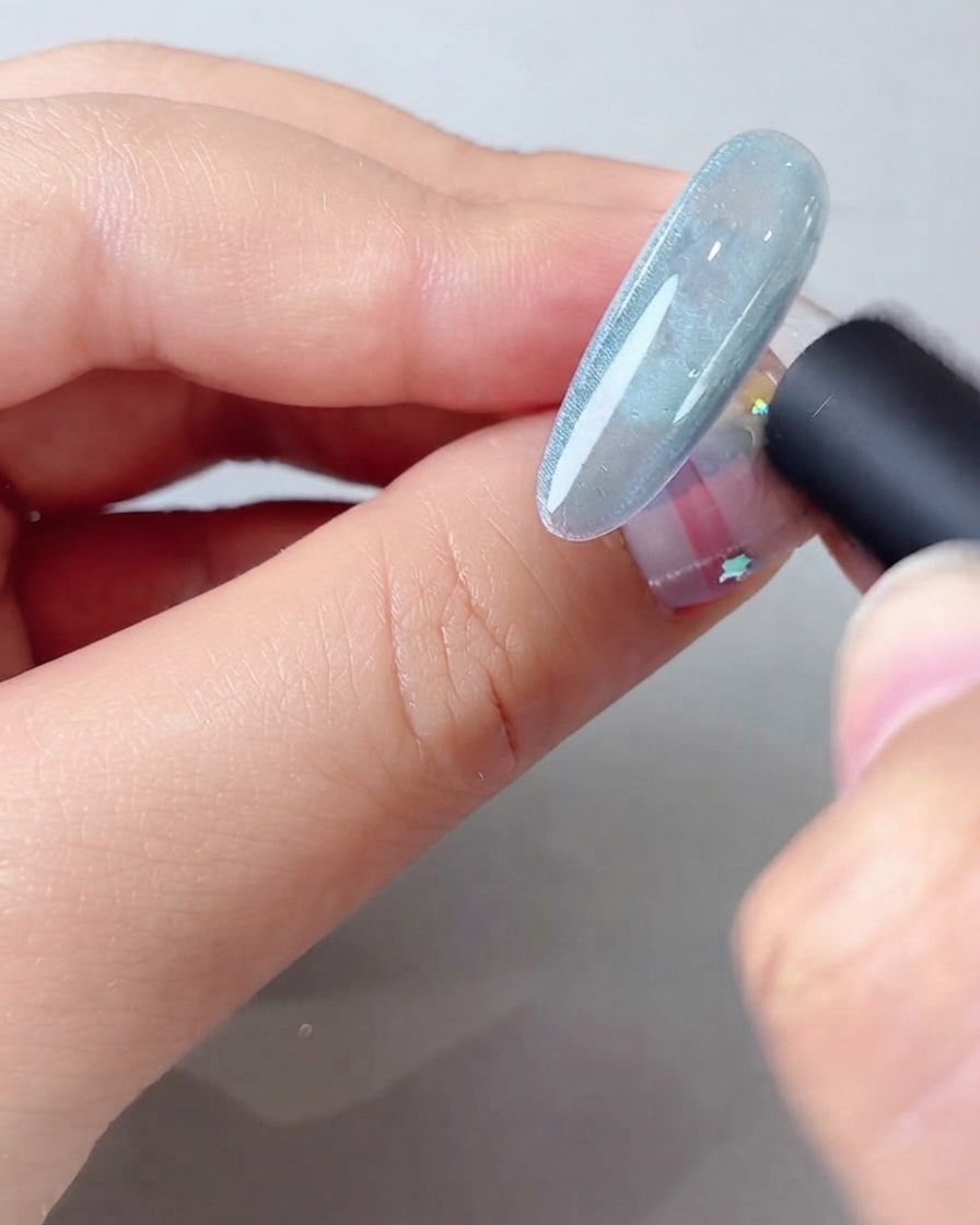 A magnetic tool held close to a blue cat eye gel nail to form a wide shimmering light beam.