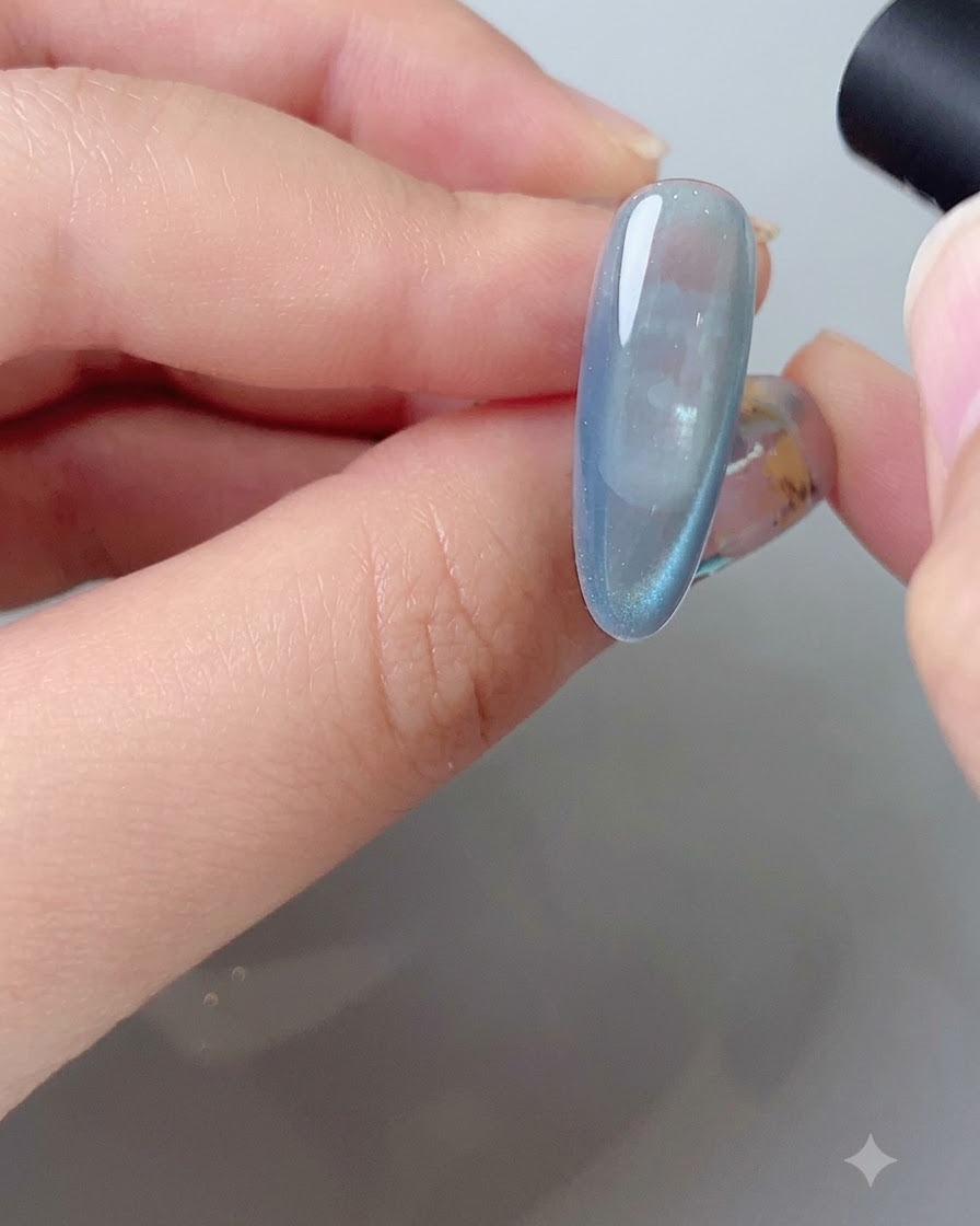 A magnetic tool shaping the side reflection arc on a blue cat eye gel nail.