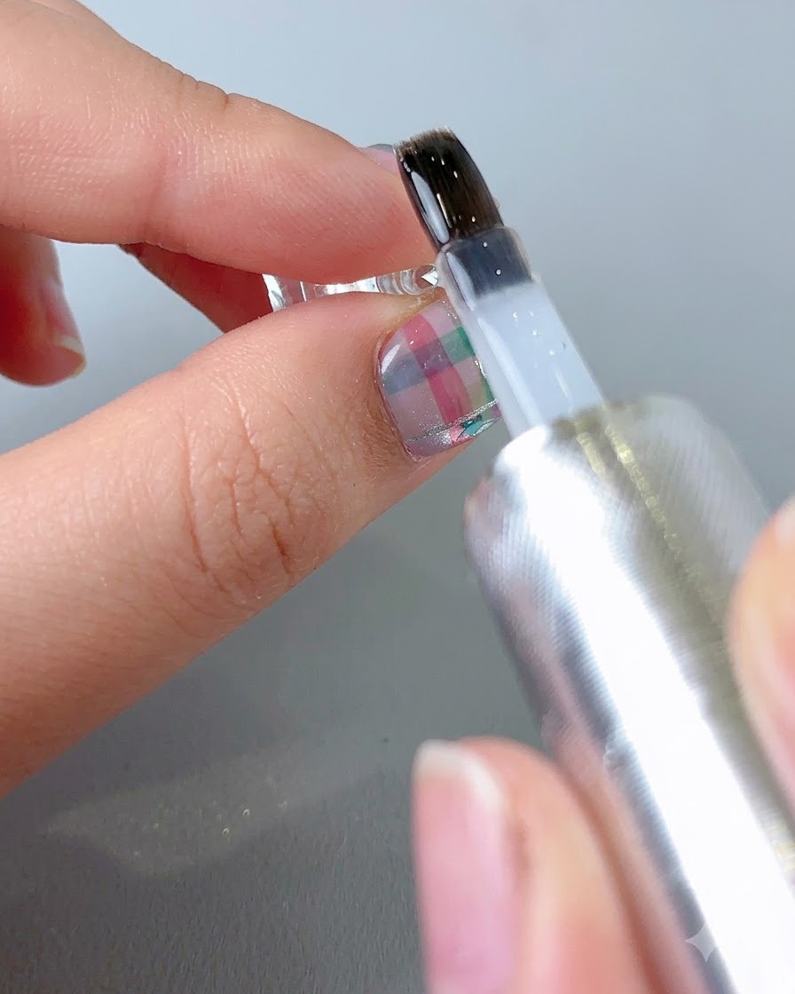 A brush applying a clear, glossy top coat onto the surface of a finished patterned nail.