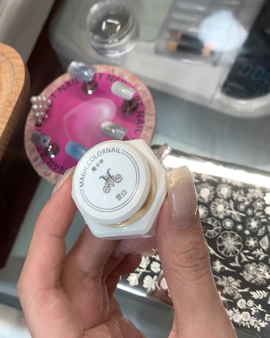 A hand holding a white bottled stamping product labeled in Asian characters with a nail stamping plate in the background.