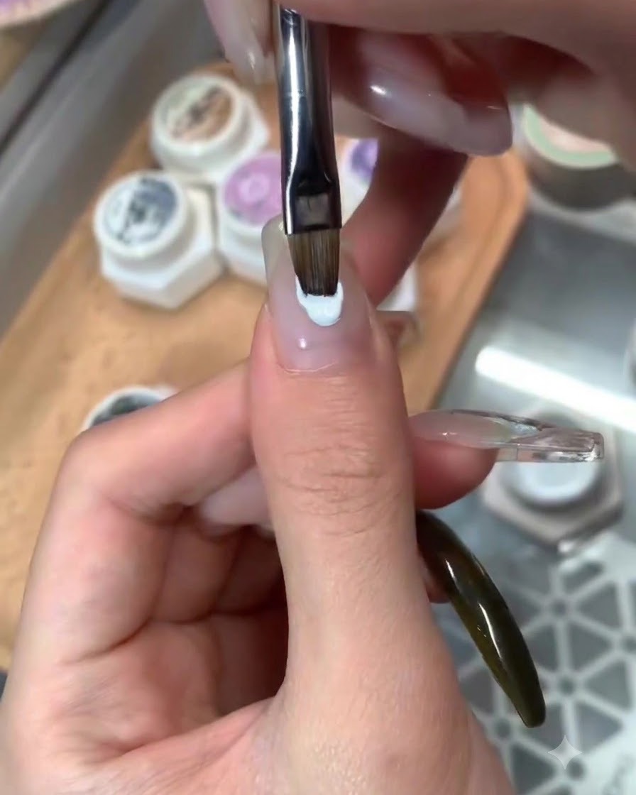 A brush applying a glossy top coat over finished blue-themed nail art.