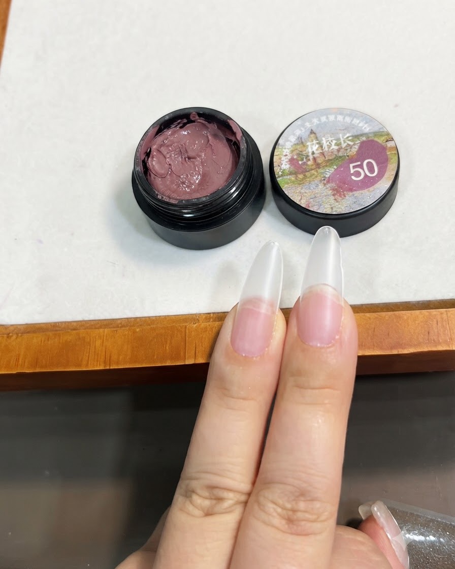 A brush holding a small amount of bean paste pink solid gel near the tip of a clear nail extension.
