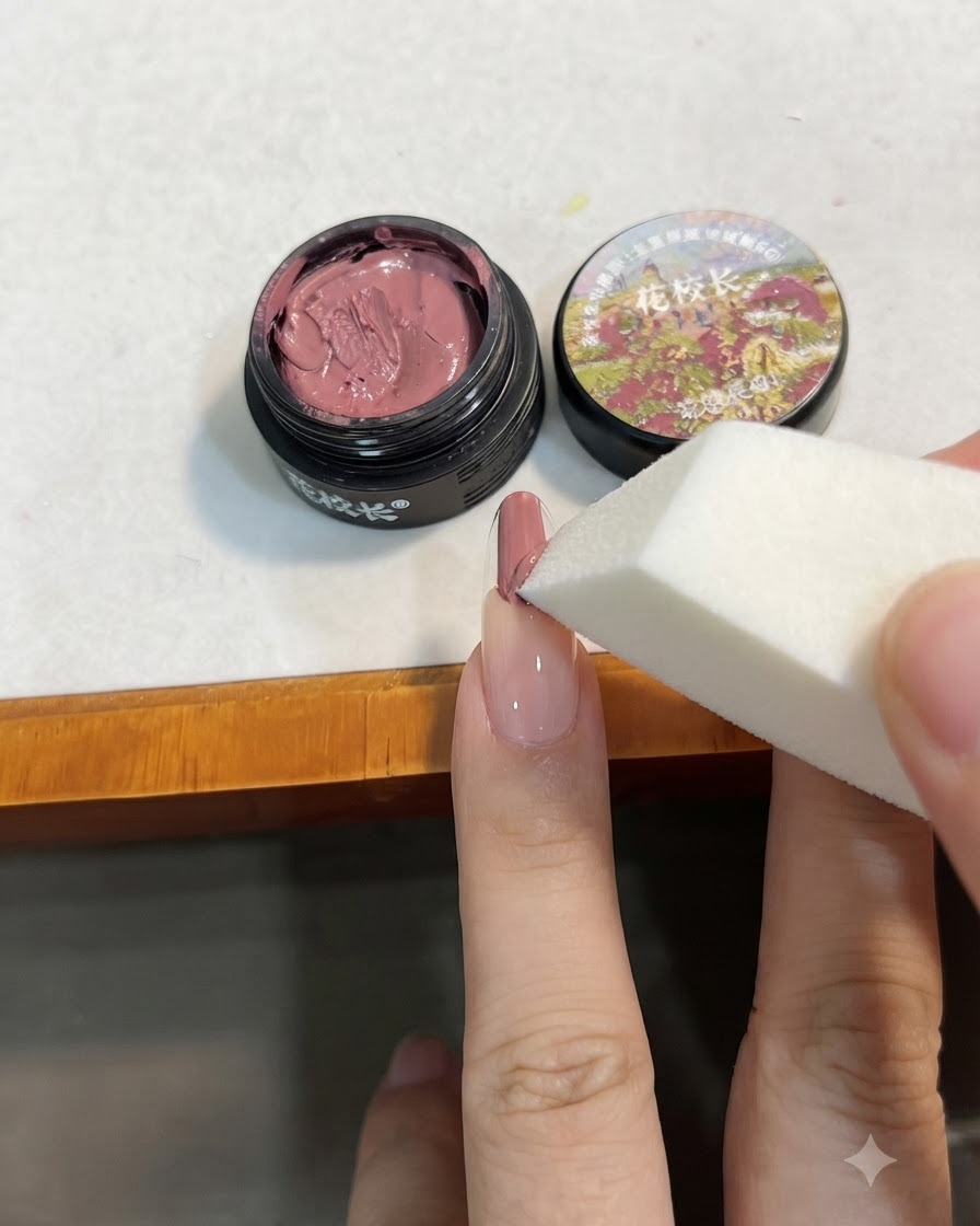A white makeup sponge tapping the pink gel on the nail to blend it downward into a gradient.