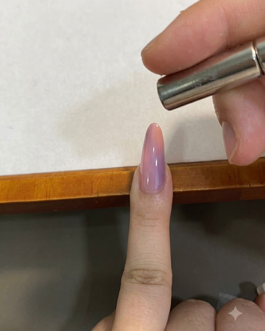 A small magnet held close above a pink gradient cat-eye nail to shape the magnetic pigment.