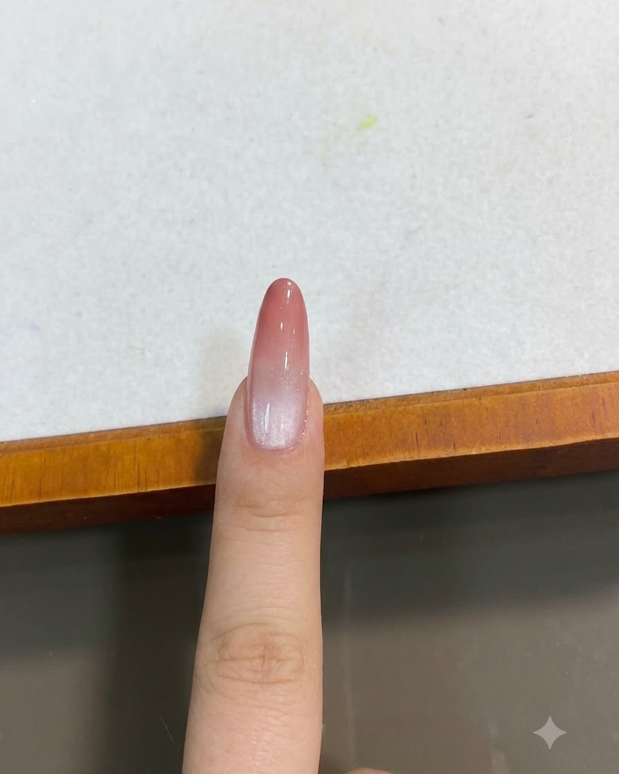 A finished peach pink gradient cat-eye nail viewed from a top-down close-up angle.