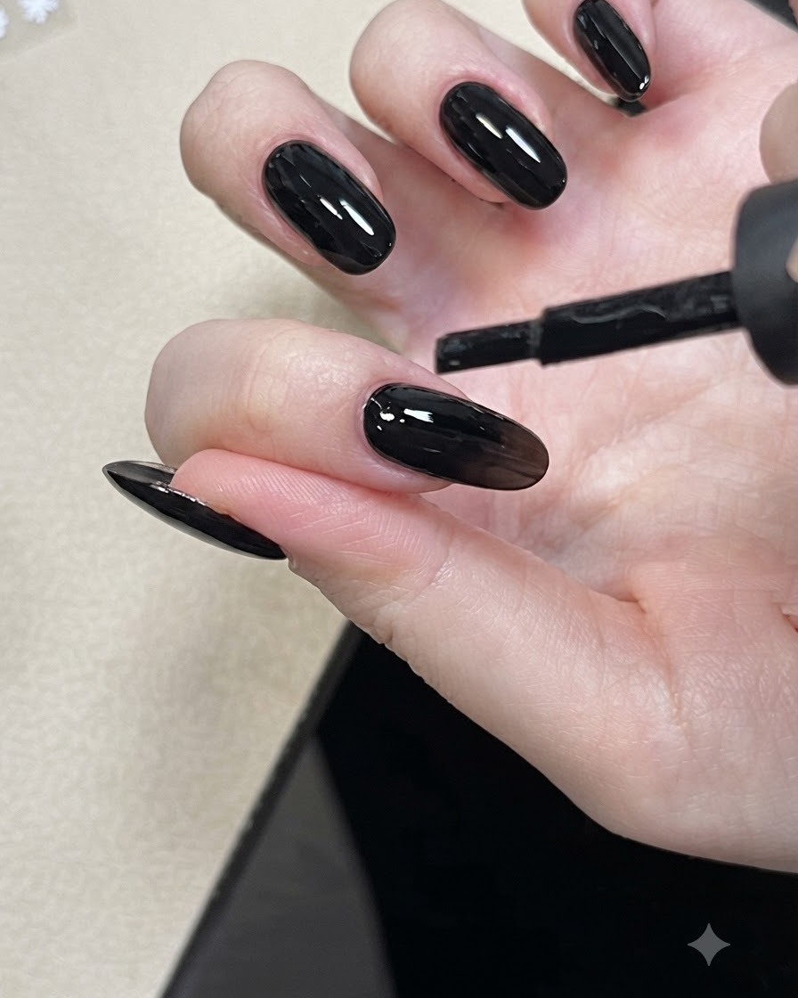 A nail brush applying nude base coat gel to a fingernail.