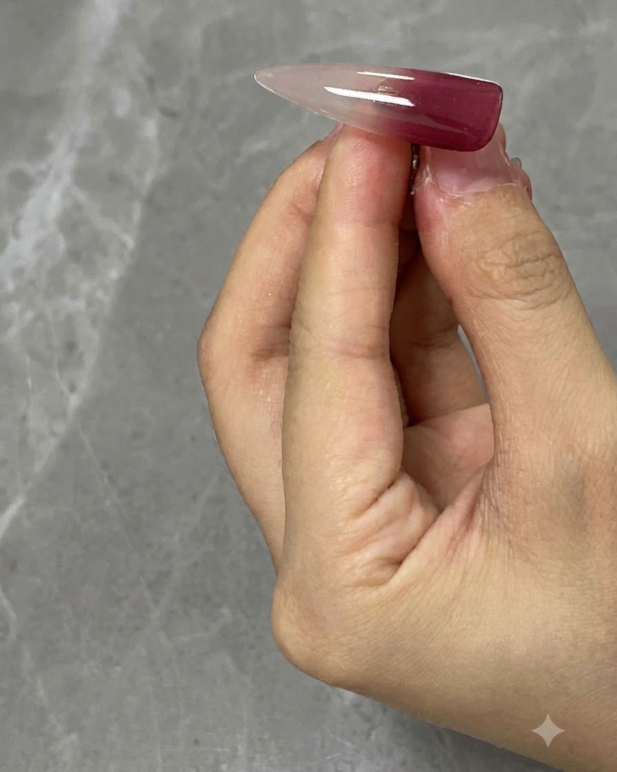 A clear practice nail tip showing a wine red application on the upper section.