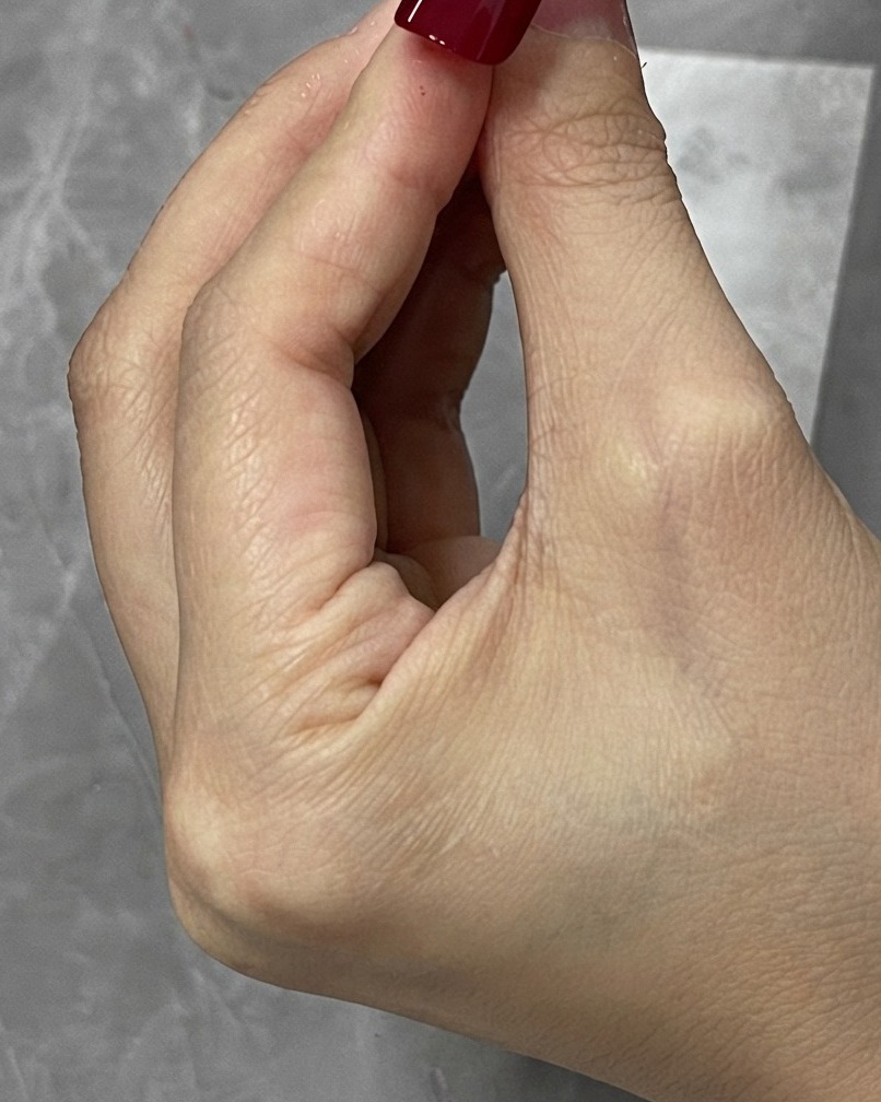 A cleanup brush wiping away stray red gel around the edges of a nail tip.