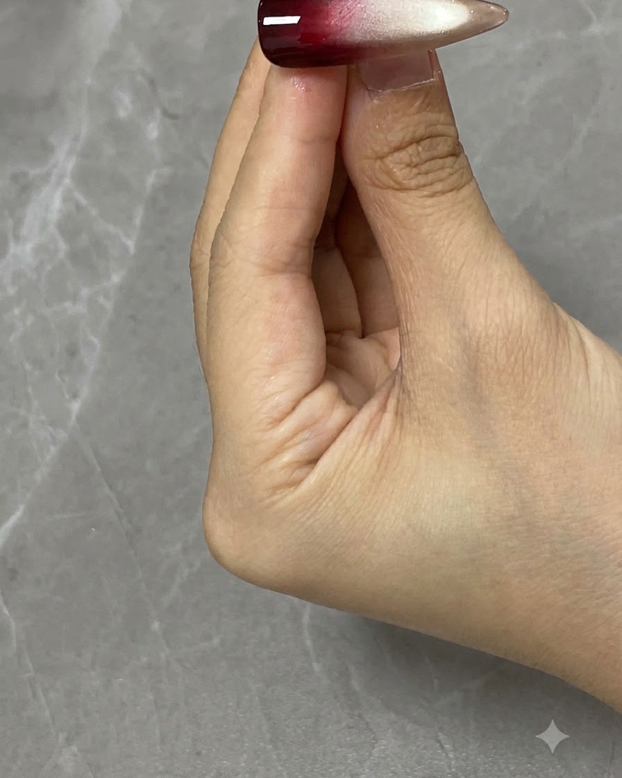 A nail art brush applying translucent red gel onto the upper half of a decorated nail.