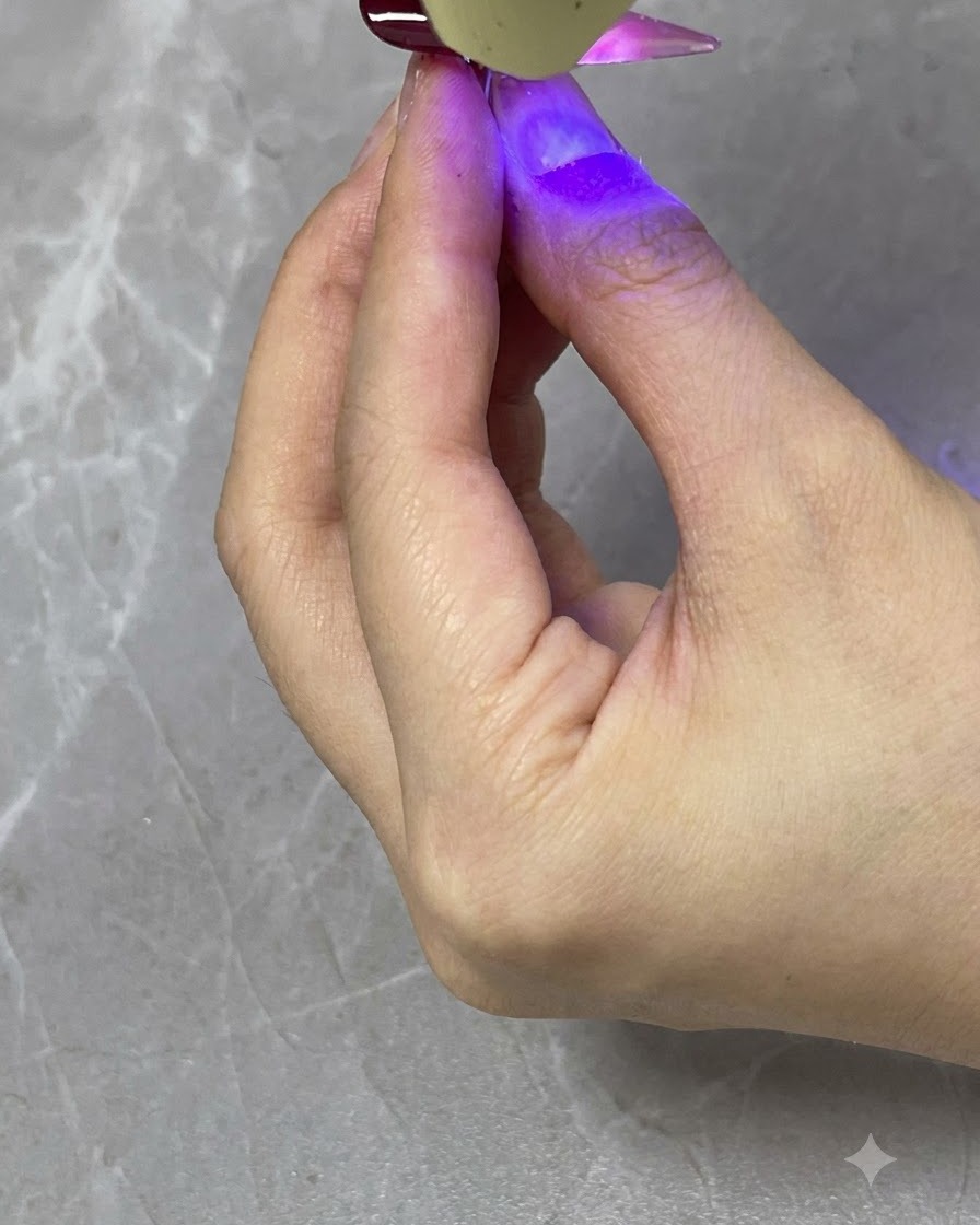A handheld UV/LED lamp curing a translucent red gradient layer on a finished nail.