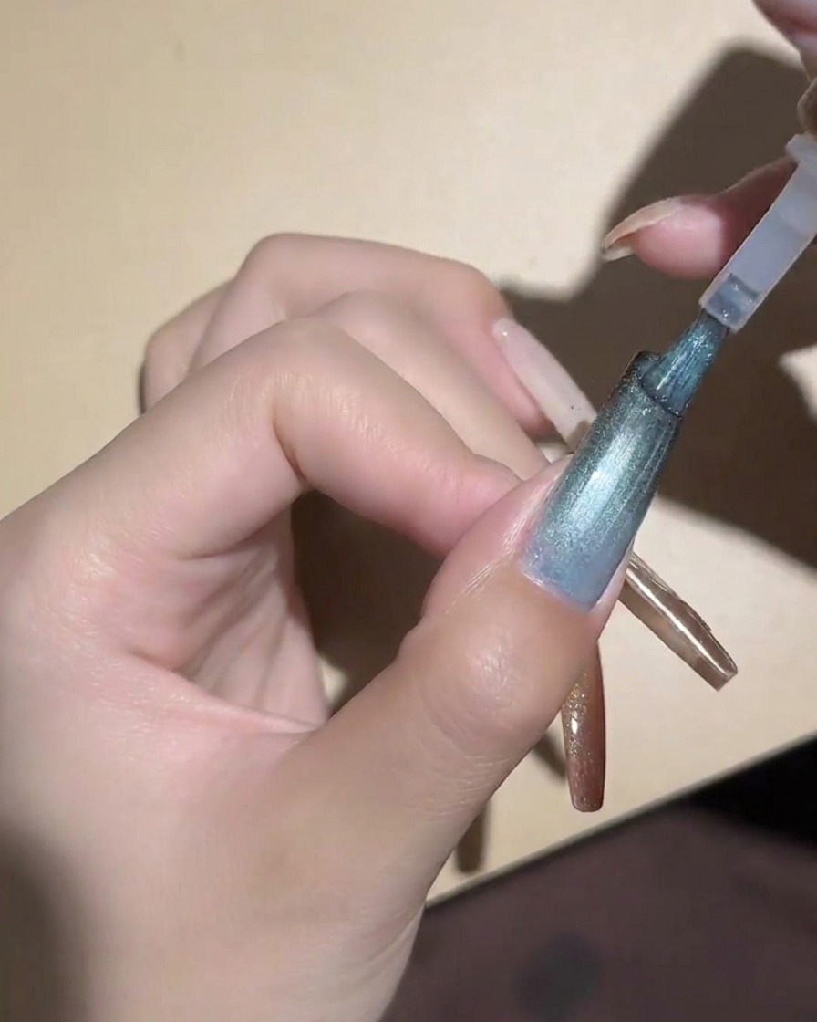 A cylindrical magnet held close to a blue cat-eye nail to magnetize the particles.