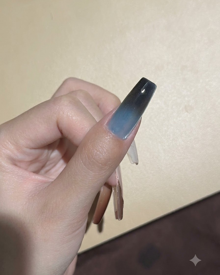 A sponge dabbing dark pigment onto the upper tip of a gel nail to deepen the ombre transition.