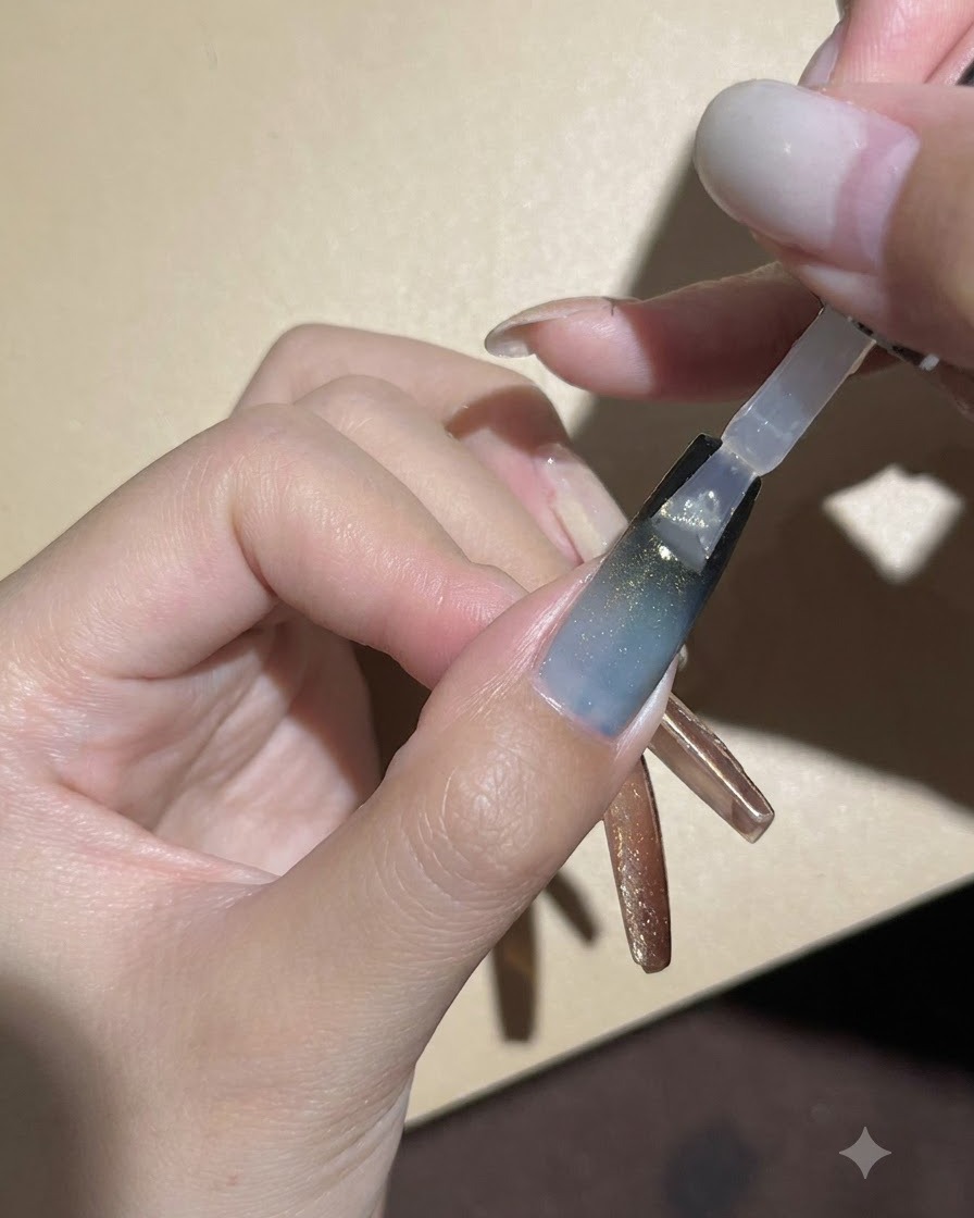 A nail brush applying a clear glossy top coat over the dark gradient and cat-eye gel nail.