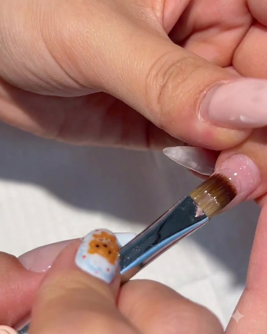 A close-up of a nail brush applying clear builder gel onto a prepped fingernail.