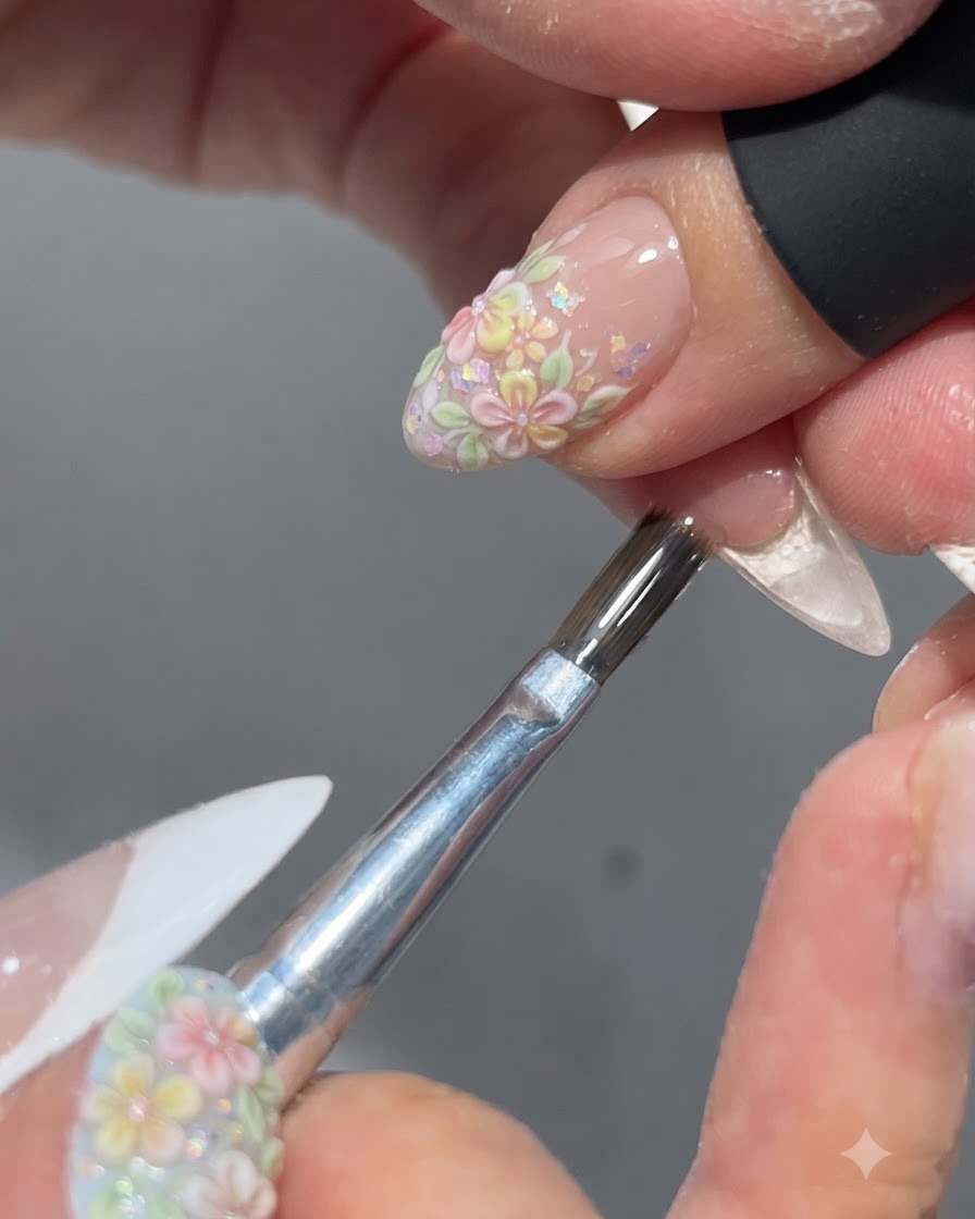 A brush applying a glossy top coat over a completed floral nail design.