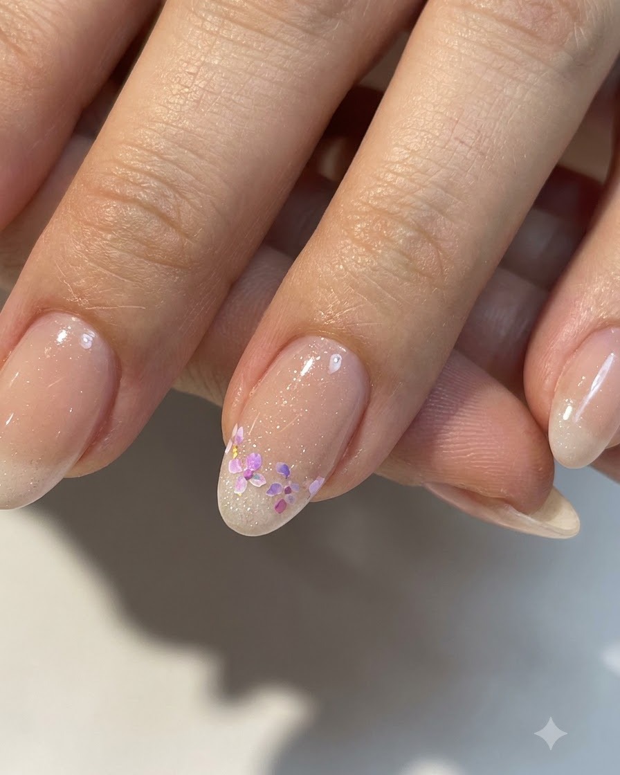 A close-up of completed small floral nail art on a glossy nude base with refined details.