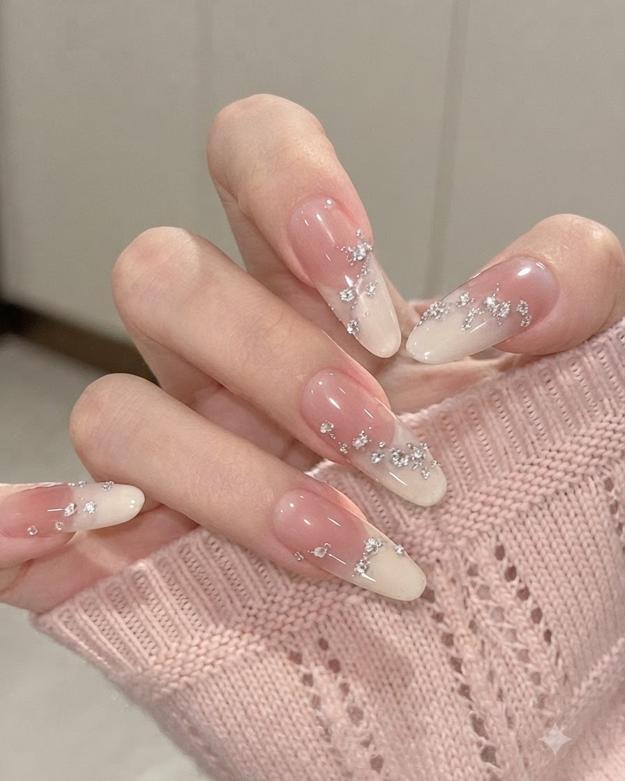 A close-up view of almond-shaped gradient nails with fingers gently flexed, highlighting embedded silver foil flakes and tiny rhinestones.