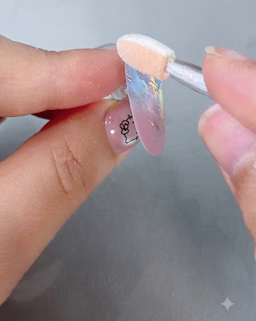 A sponge eyeshadow applicator buffing iridescent magic mirror powder onto a pastel-colored nail tip.