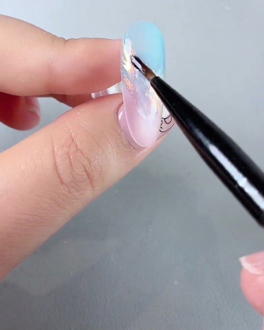 A fine nail art brush applying sparkling iridescent glitter details onto a pastel gradient nail.