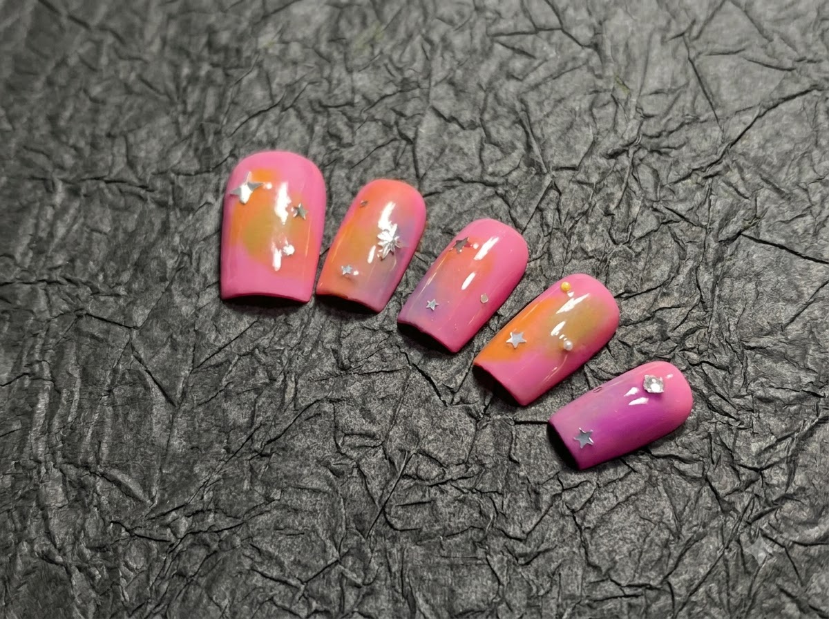 A panning shot capturing the full set of five peach and purple gradient nails with silver star accents.