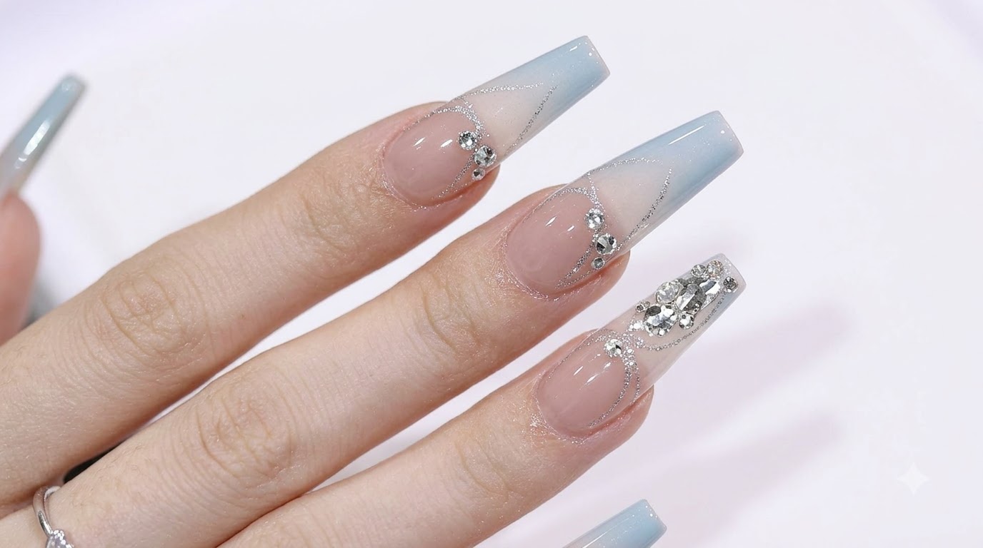 Long coffin-shaped nails featuring a soft blue-to-nude gradient, accented with sparkling rhinestones and silver glitter details.