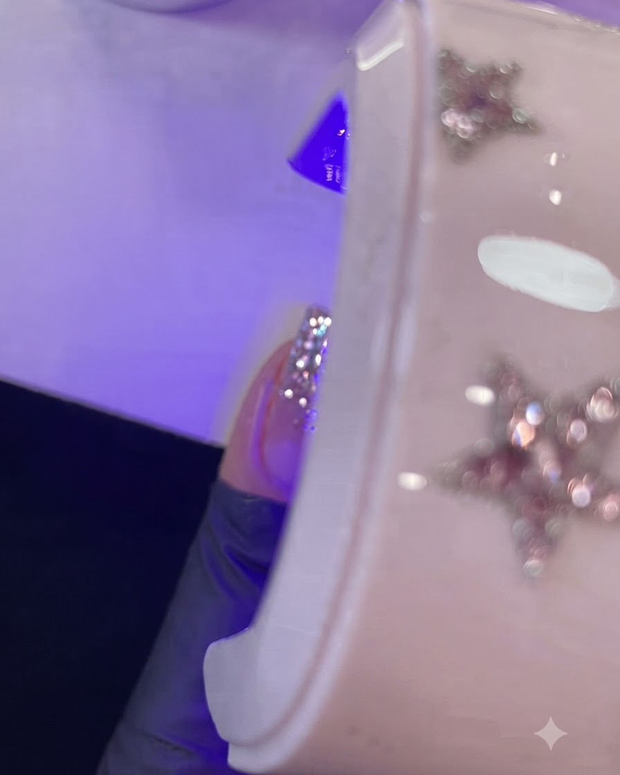 A close-up of a finger with wet gel being cured under a purple mini UV/LED lamp.