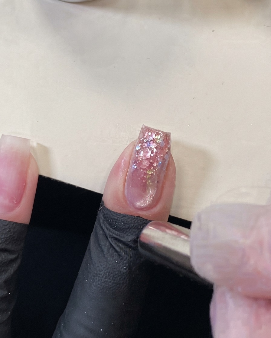 A cylindrical magnet held near the tip of a pink glitter nail to push the magnetic cat eye effect.