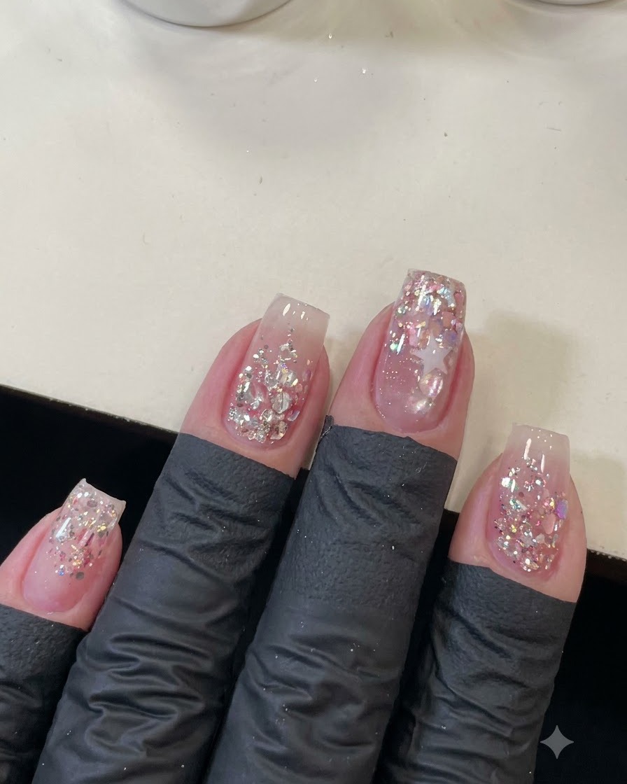 An overhead shot of four manicured nails decorated with sparkling pink sequins and a star outline.