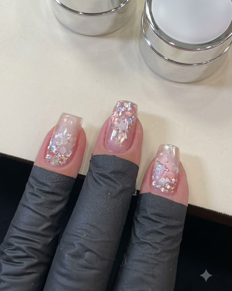 A close-up view of a hand applying top coat over the detailed star and sequin nail art.