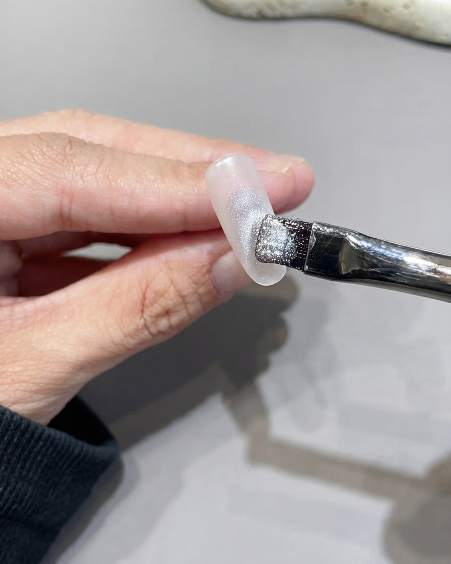 A flat brush applying sparkly silver cat eye gel across the surface of a nail.