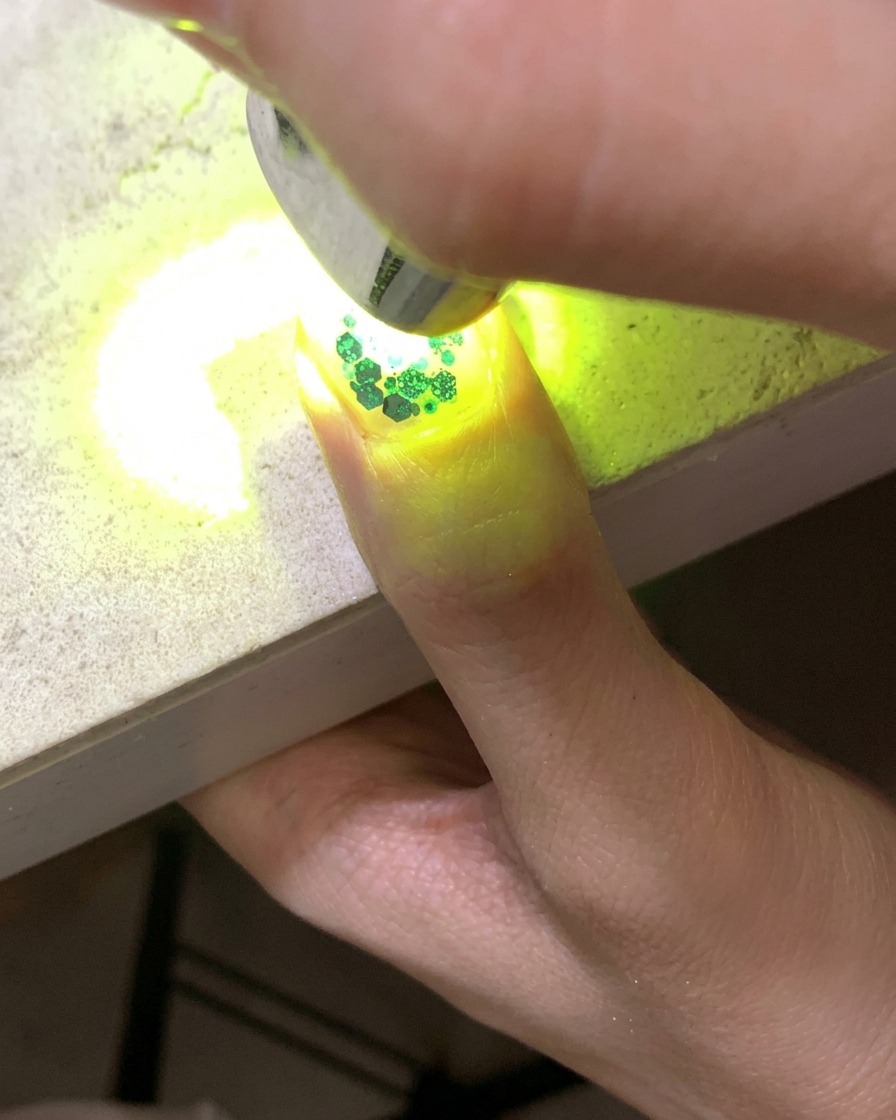A mini UV lamp curing a nail adorned with glitter and hollow star sequins.