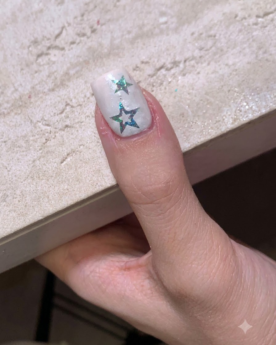 A fingernail with star stickers positioned under a small portable LED curing lamp.