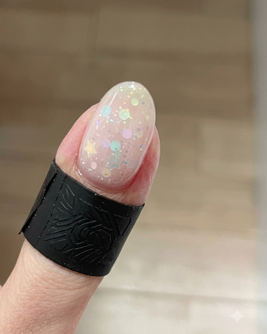 A close-up of a fingernail showing a glowing cat-eye gel effect with bright shimmer concentrated at the tip over star glitters.