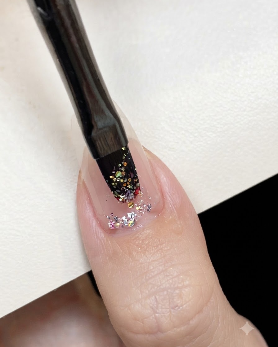 A flat gel brush dabbing pink holographic glitter gel onto the center of a prepped nail.