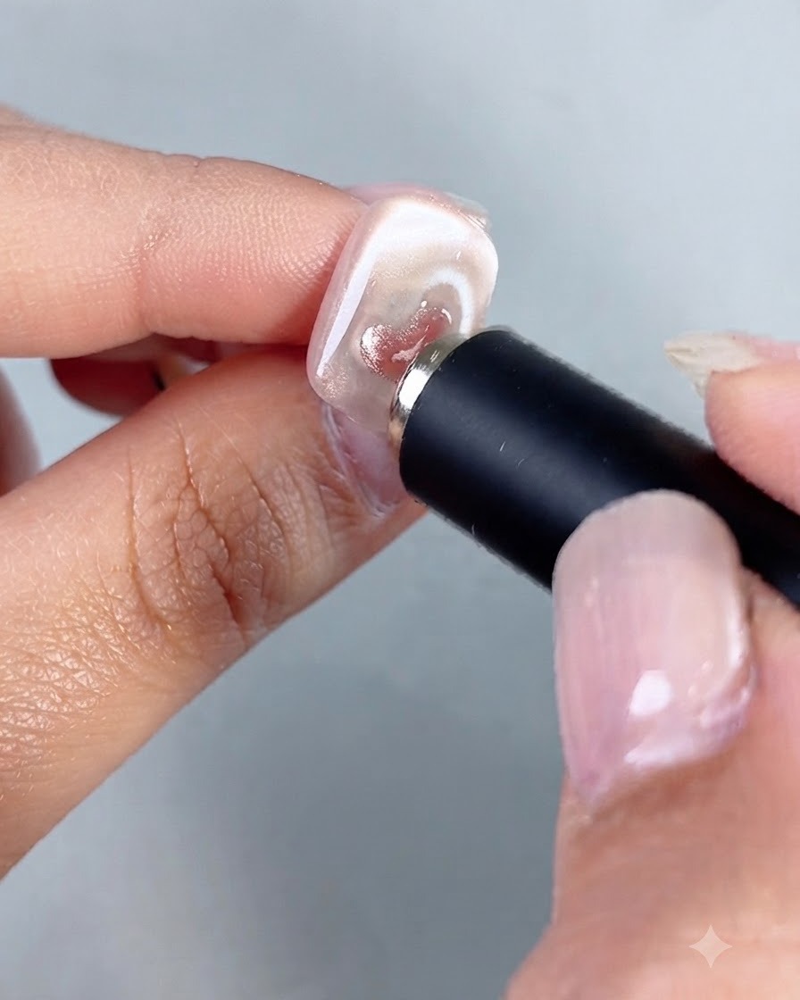 A cylindrical magnet tool being held close to a nail, concentrating the shimmer inside a small painted cat-eye heart.
