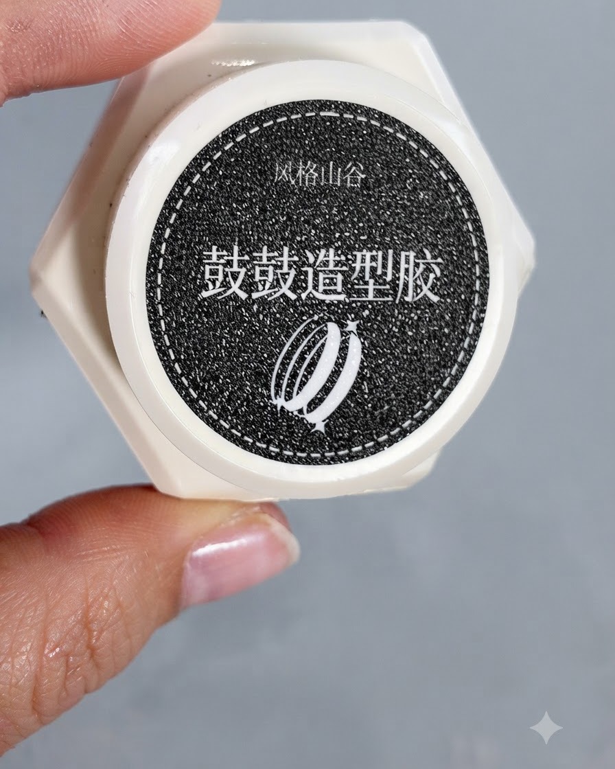 Fingers holding a small white pot of Style Valley chunky shaping gel.