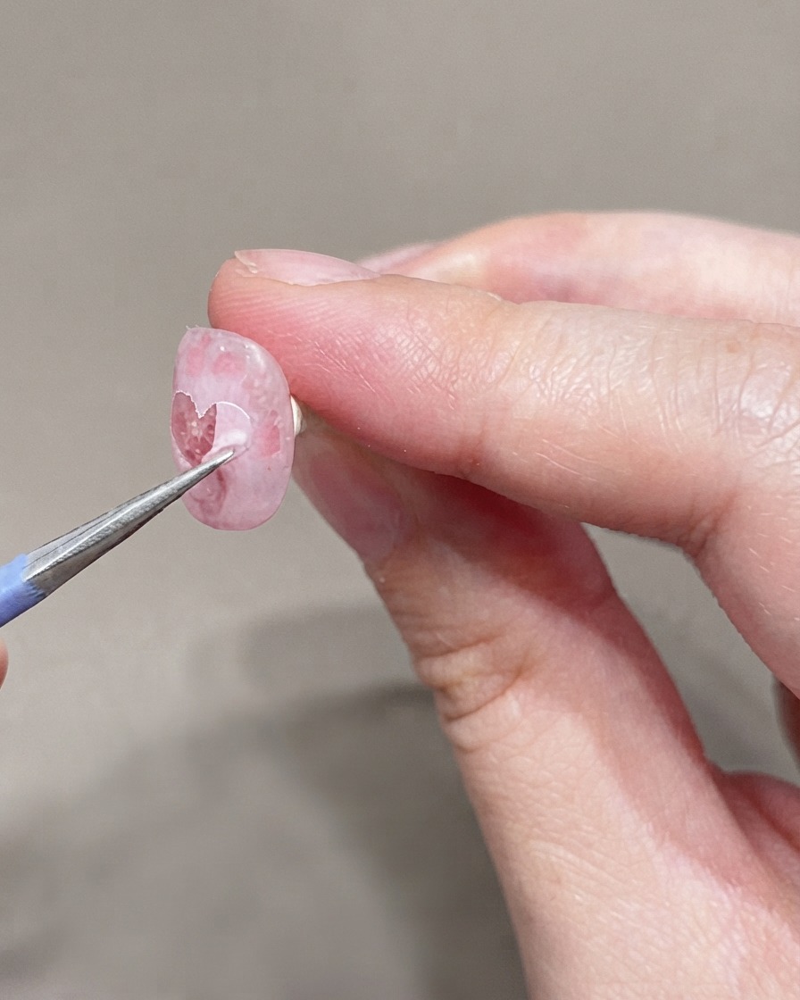 A fine brush applying a second coat of very light pink gel polish onto the prepped nail.
