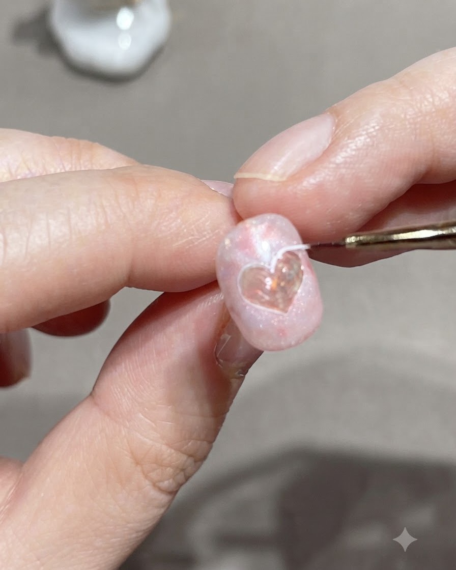 A fine liner brush tracing the outer edge of a heart sticker on a pink gel nail.